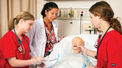 Two student nurses practice skils on a dummy patient in a hospital bed